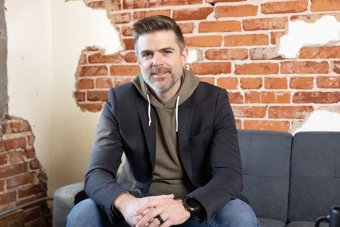 Jared Auld sitting on a sofa in front of an exposed brick wall